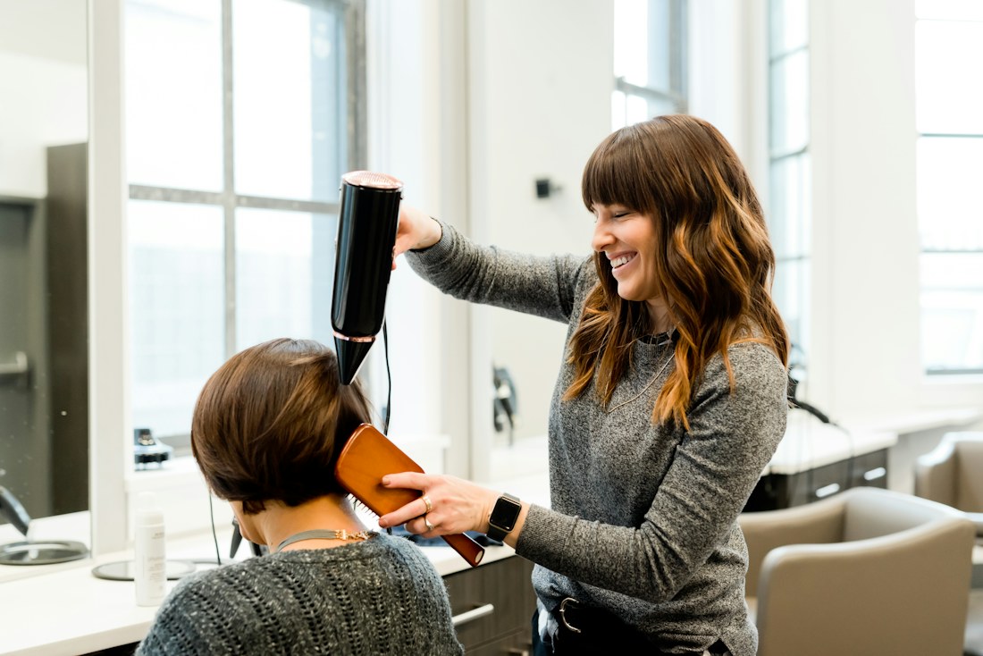 A hairstylist carefully blow-drying a customer’s hair in a light-filled salon